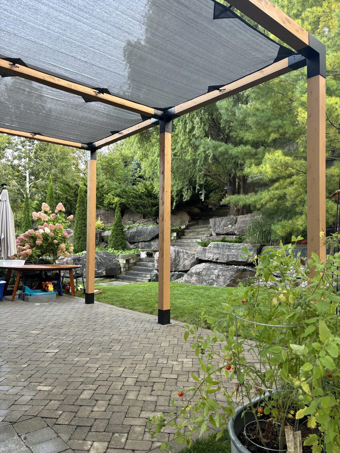 Backyard pergola over an interlocking stone patio, with stone steps and landscaping, built by Kopman Build
