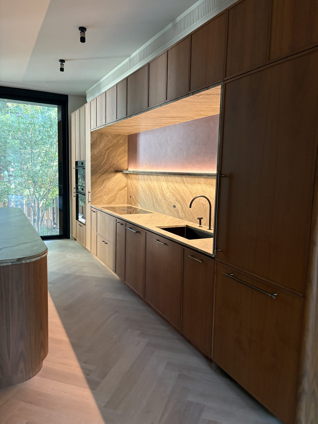Custom walnut kitchen with full-height cabinetry, lit stone backsplash and herringbone floor in Roncesvalles, Toronto, built by Kopman Build in 2022